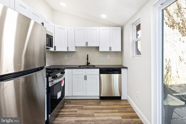 kitchen with sink, white cabinetry, vaulted ceiling, light wood-type flooring, and appliances with stainless steel finishes