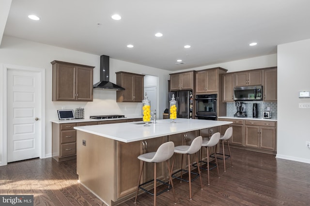 kitchen with a center island with sink, dark hardwood / wood-style floors, wall chimney exhaust hood, black appliances, and a breakfast bar area