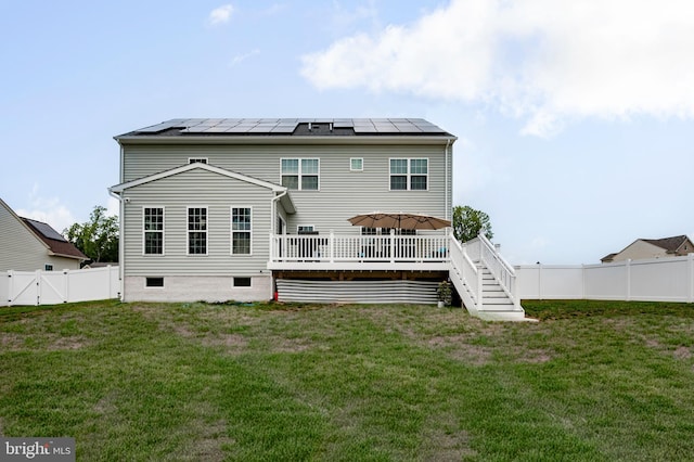 rear view of house with a yard, a wooden deck, and solar panels