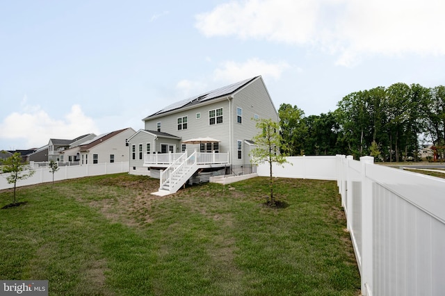 rear view of property featuring a deck, a yard, and solar panels