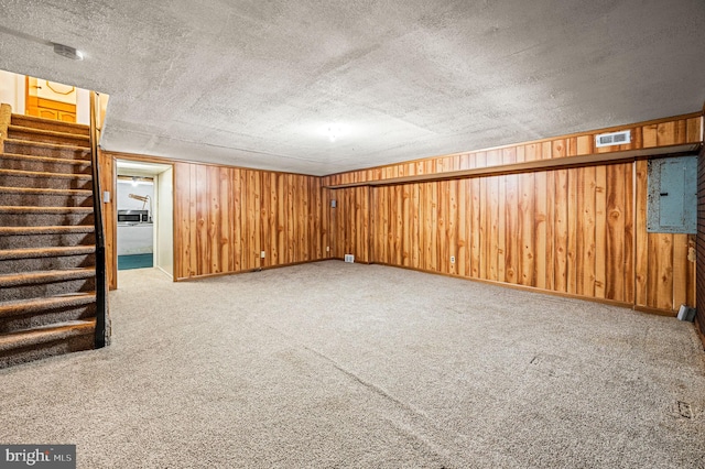 basement featuring wooden walls, electric panel, carpet, and a textured ceiling