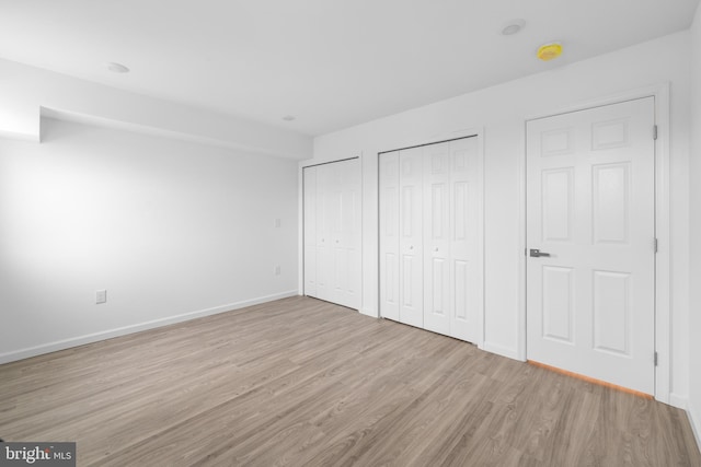 unfurnished bedroom featuring two closets and light hardwood / wood-style floors