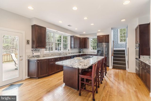 kitchen with visible vents, light wood-style flooring, a kitchen island, appliances with stainless steel finishes, and a breakfast bar area