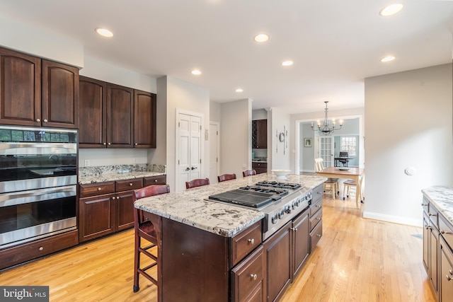 kitchen featuring stainless steel appliances, a kitchen bar, light wood-style floors, and light stone countertops