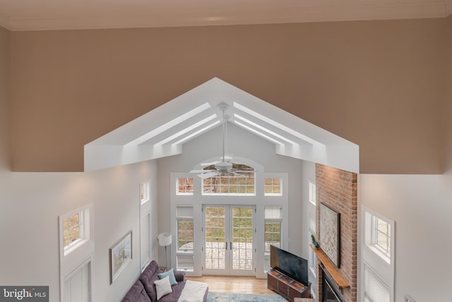 living room featuring a ceiling fan, high vaulted ceiling, light wood-style flooring, french doors, and a brick fireplace