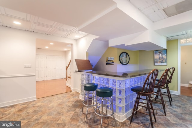 bar featuring baseboards, a bar, stairs, and stone finish floor