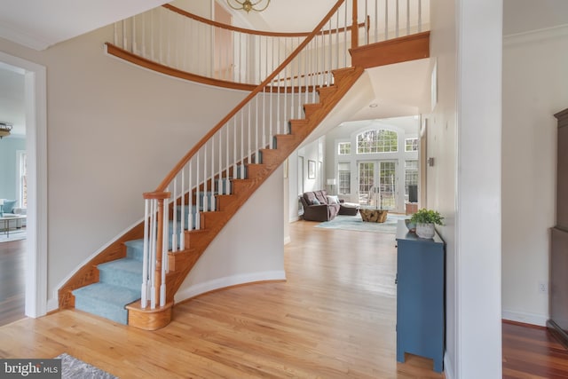 staircase featuring a high ceiling, wood finished floors, baseboards, and ornamental molding