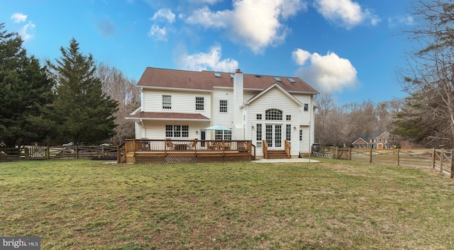 rear view of property featuring a wooden deck, a yard, a fenced backyard, a chimney, and french doors