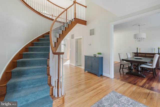 stairs featuring wood finished floors, visible vents, a towering ceiling, and baseboards