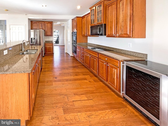 kitchen with sink, stone counters, wine cooler, black appliances, and light wood-type flooring