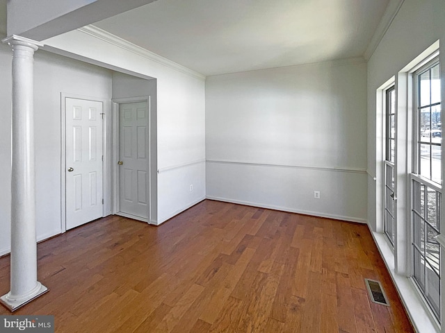 spare room featuring ornate columns, crown molding, and dark wood-type flooring