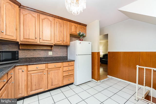 kitchen featuring light tile patterned flooring, an inviting chandelier, vaulted ceiling, white refrigerator, and dark stone counters