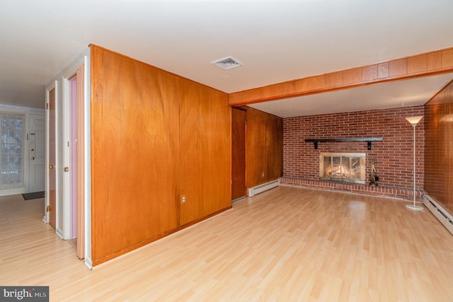 unfurnished living room with wood walls, light hardwood / wood-style floors, a brick fireplace, and a baseboard heating unit