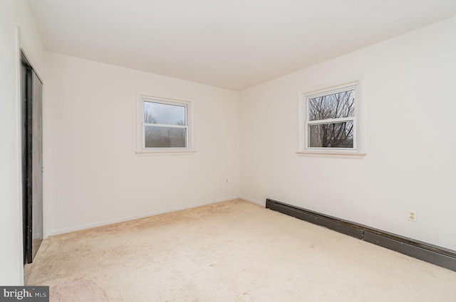 spare room featuring a baseboard heating unit and light carpet