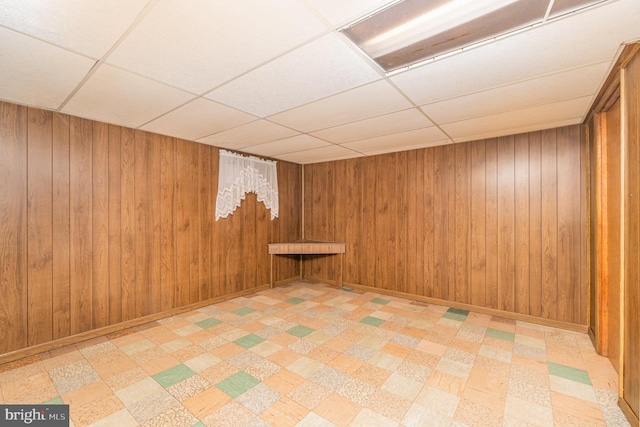 basement featuring a drop ceiling and wood walls