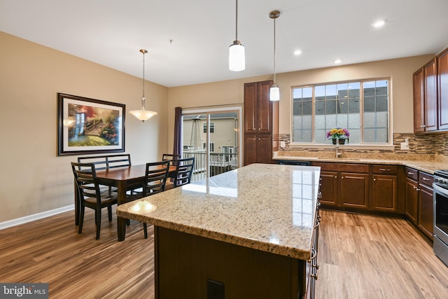 kitchen featuring decorative backsplash, light stone counters, a center island, light wood-style floors, and a sink