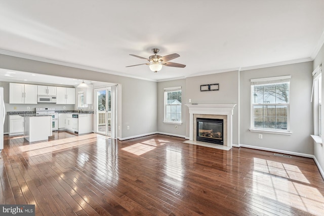 unfurnished living room with sink, crown molding, dark wood-type flooring, ceiling fan, and a fireplace