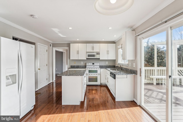 kitchen featuring white appliances, crown molding, white cabinetry, dark stone countertops, and a center island