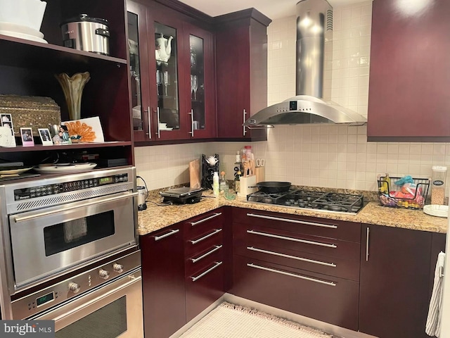 kitchen with tasteful backsplash, wall chimney range hood, light stone counters, and stainless steel appliances