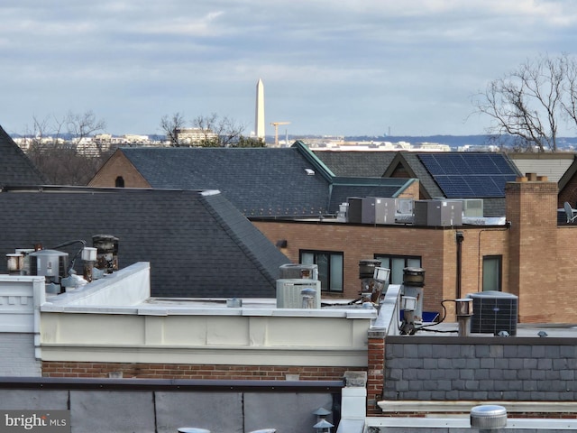 exterior space featuring central AC, brick siding, and roof with shingles