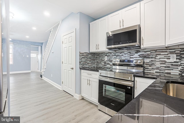 kitchen with white cabinetry, dark stone counters, stainless steel appliances, light hardwood / wood-style floors, and backsplash