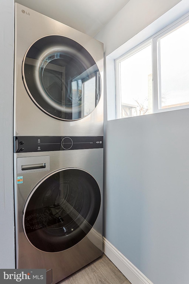 laundry room with hardwood / wood-style flooring and stacked washing maching and dryer