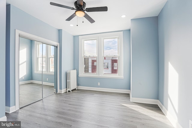 unfurnished bedroom with ceiling fan, radiator heating unit, light wood-type flooring, and a closet