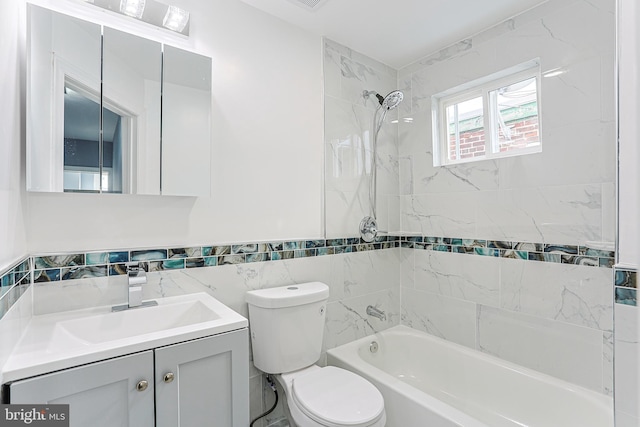 full bathroom featuring tiled shower / bath, vanity, toilet, and tile walls