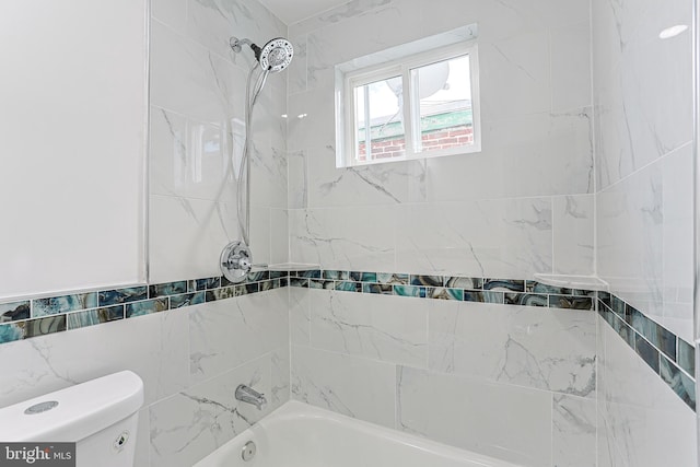 bathroom featuring tiled shower / bath, toilet, and tile walls