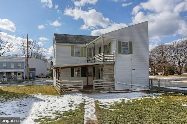 snow covered rear of property with covered porch and a lawn