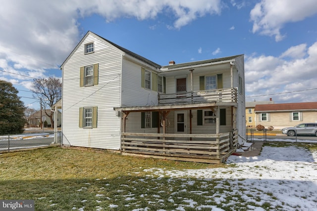 snow covered house featuring a balcony and a yard