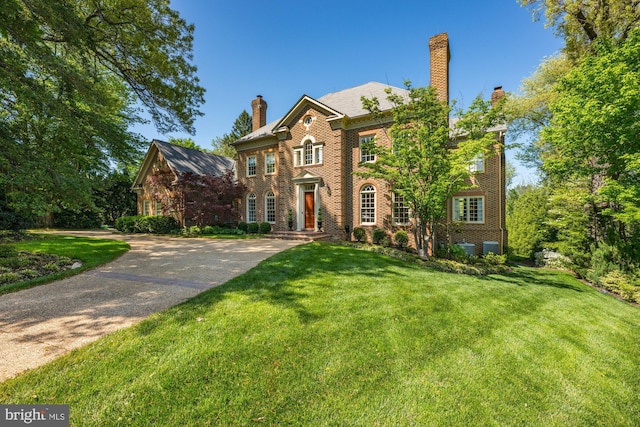 view of front of house with brick siding, a chimney, and a front lawn
