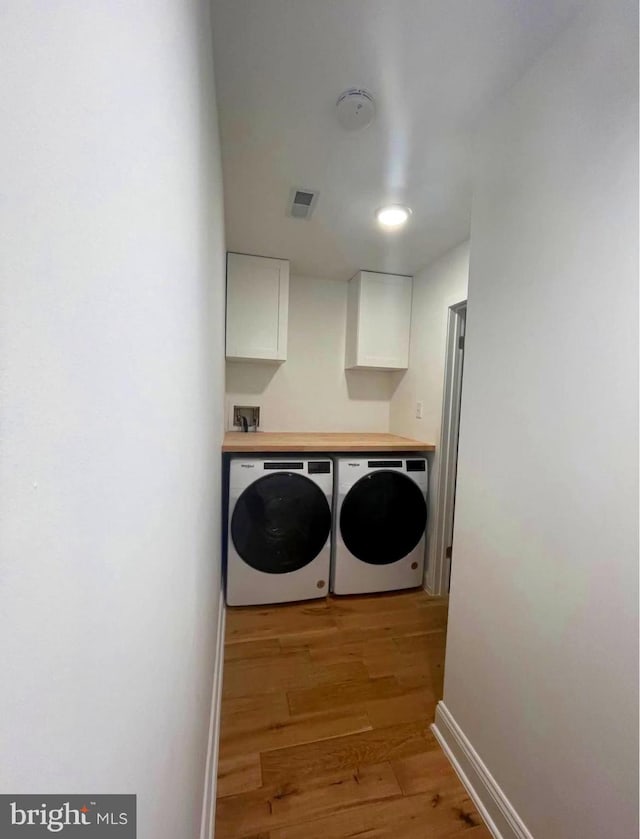 laundry room featuring light wood-style flooring, separate washer and dryer, visible vents, baseboards, and cabinet space