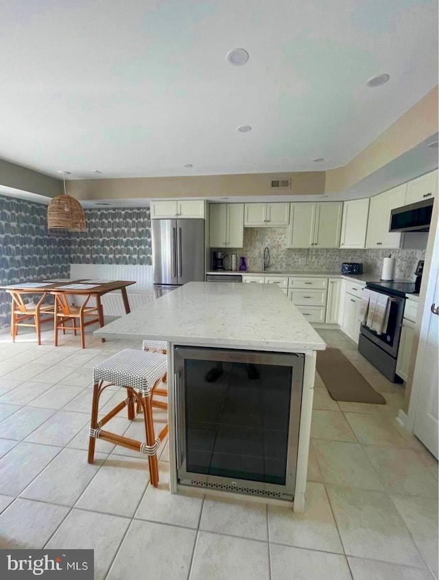 kitchen with stainless steel appliances, wine cooler, light tile patterned floors, and light stone countertops