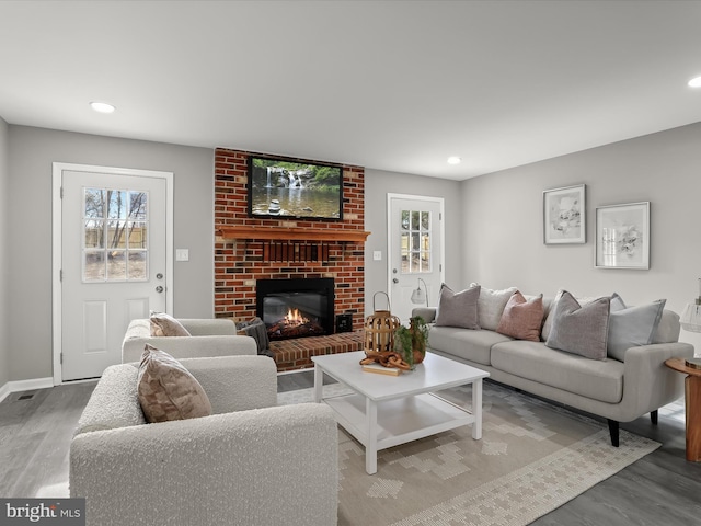 living room with a brick fireplace, plenty of natural light, baseboards, and wood finished floors