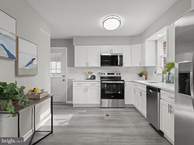 kitchen with a sink, white cabinetry, light countertops, appliances with stainless steel finishes, and light wood finished floors