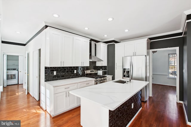 kitchen with stainless steel gas range oven, wall chimney exhaust hood, washer / dryer, sink, and a kitchen island with sink