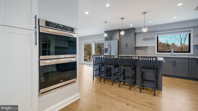 kitchen with a kitchen breakfast bar, light wood-style floors, appliances with stainless steel finishes, backsplash, and gray cabinets