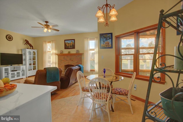 dining area featuring ceiling fan with notable chandelier and a brick fireplace