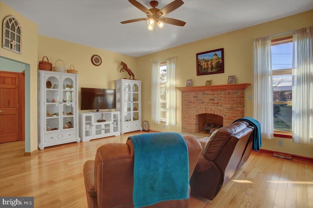 living room with hardwood / wood-style flooring, a brick fireplace, and ceiling fan