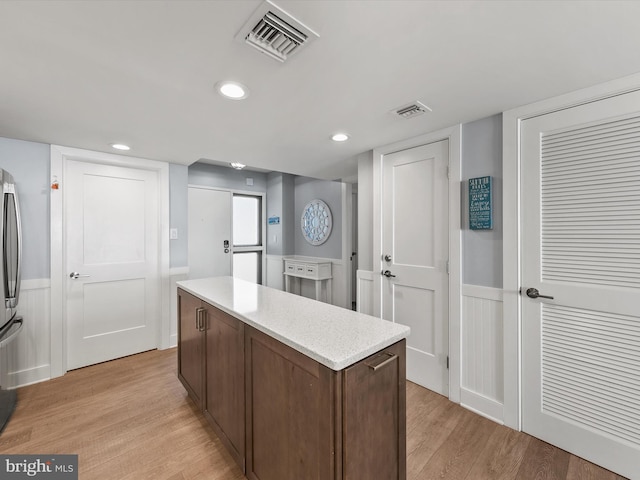 kitchen with stainless steel refrigerator, a kitchen island, and light wood-type flooring