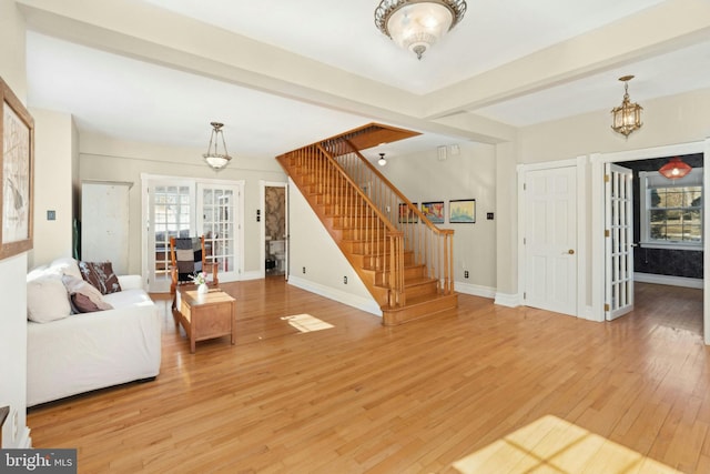 unfurnished living room with baseboards, french doors, stairway, light wood-type flooring, and beam ceiling