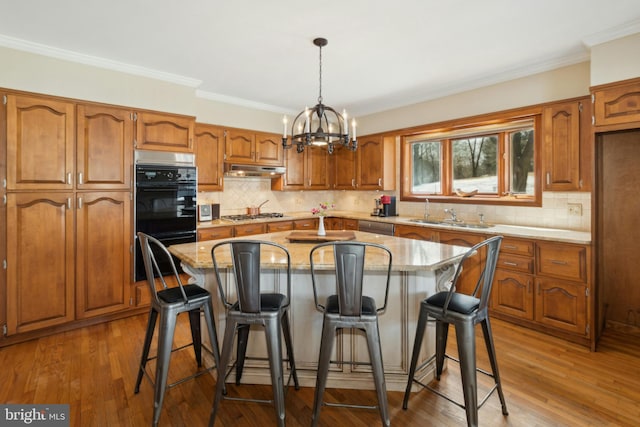 kitchen with stainless steel appliances, brown cabinetry, and under cabinet range hood