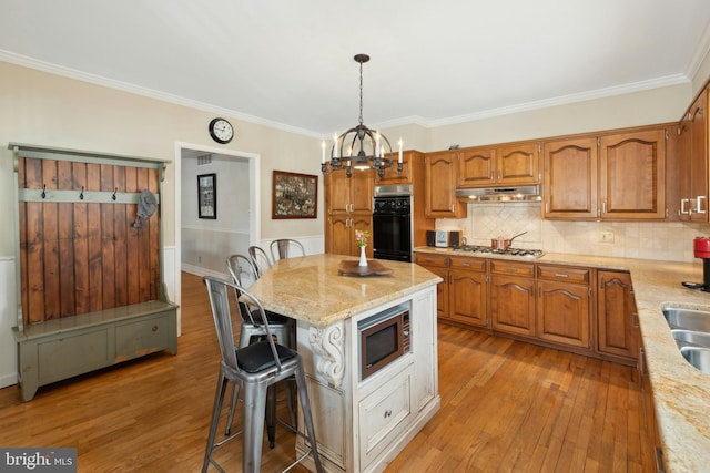 kitchen featuring appliances with stainless steel finishes, brown cabinets, light wood-style floors, and under cabinet range hood