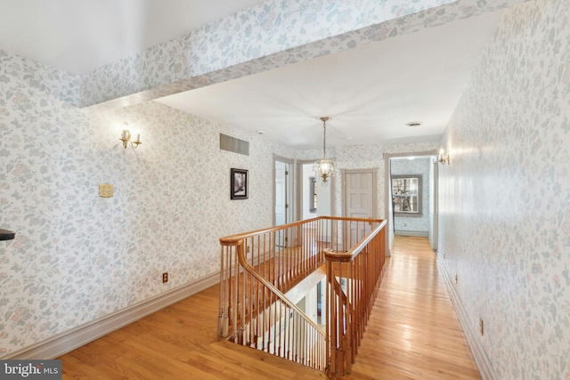 corridor featuring visible vents, light wood-style flooring, an upstairs landing, baseboards, and wallpapered walls