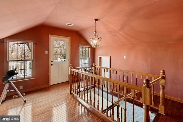 interior space with visible vents, wood-type flooring, vaulted ceiling, an upstairs landing, and a chandelier