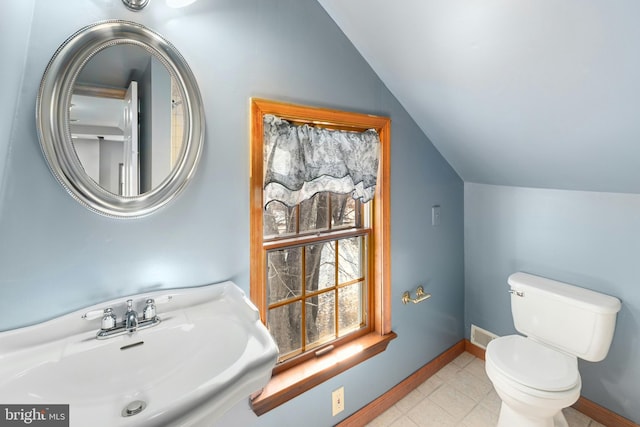 half bath featuring lofted ceiling, toilet, a sink, visible vents, and baseboards