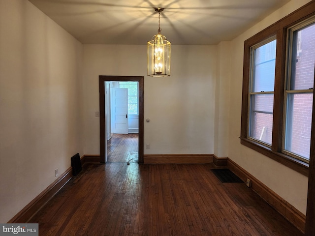 spare room featuring dark wood-type flooring, plenty of natural light, and a chandelier