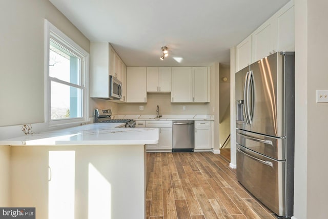 kitchen featuring sink, light wood-type flooring, kitchen peninsula, stainless steel appliances, and white cabinets