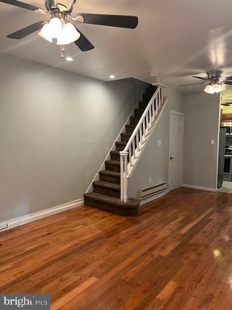 stairway featuring baseboard heating, ceiling fan, and hardwood / wood-style flooring